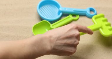 Plastik tırmıklı kadın kumda çizgiler çiziyor, yakın plan. Çocuklar için plaj oyuncakları