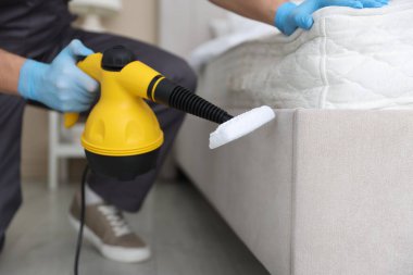 Haşere kontrol işçisi yatağı temizliyor, kapalı alanda buhar temizleyicisiyle, yakın plan