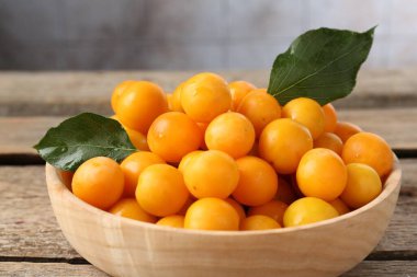 Olgun sarı kiraz erikleri ve yapraklar ahşap masada, yakın plan.