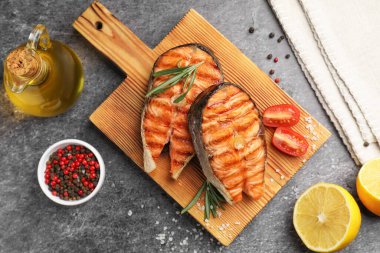 Limonlu, domatesli ve biberiyeli ızgara somon bifteği gri masada, düz yatıyordu.