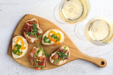 Beyaz masada servis edilen prosciutto ve şaraplı leziz bruschettalar, düz yerde.