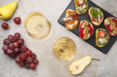 Bardakta beyaz şarap, bruschette ve gri masada meyveler.