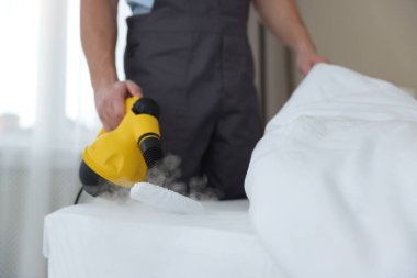 Haşere kontrol işçisi yatağı temizliyor, kapalı alanda buhar temizleyicisiyle, yakın plan