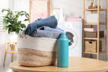 Çamaşır sepetinde giysiler ve ahşap masada bir şişe deterjan.