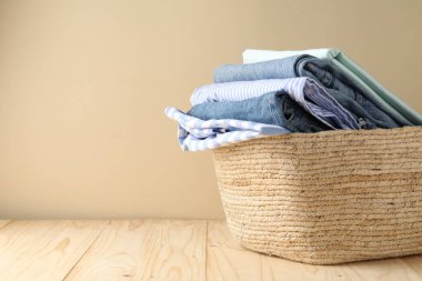 İçerideki bej duvarın yanındaki ahşap masada giysileri olan çamaşır sepeti, yakın plan. Metin için boşluk
