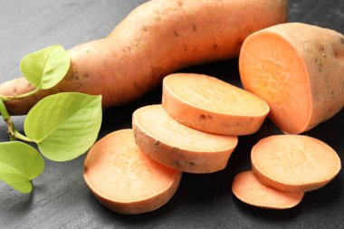 Tüm, tatlı patatesler ve yeşil yapraklı dallar koyu dokulu masa, yakın çekim