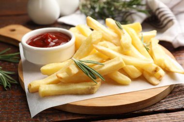 Patates kızartması ketçap ve biberiyeyle servis edilir, ahşap masada, yakın plan.
