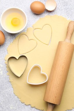Çiğ hamur, kalp şeklinde kurabiye kesiciler, yuvarlanan iğne ve yumurtalar açık gri desenli masa, düz yatıyordu.