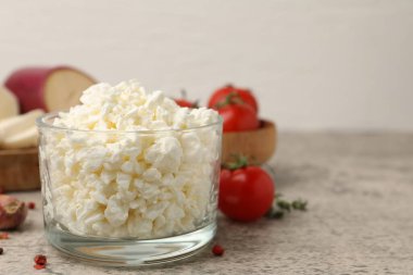 Cam kasede taze süzme peynir, gri masada domates ve baharatlar, yakın plan.