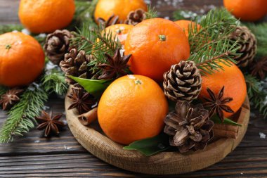 Olgun mandallar, baharatlar, köknar ağacı dalları ve tahta masanın üzerindeki koniler, yakın plan.