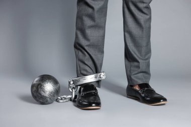 Bacağında metal top ve zincir olan iş adamı gri arka planda, yakın plan.