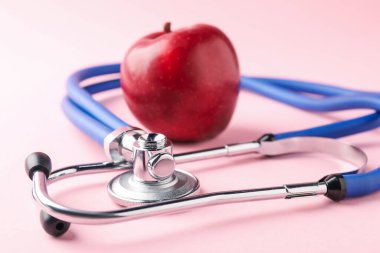 Pembe arka planda olgun elma ve steteskop, yakın plan.