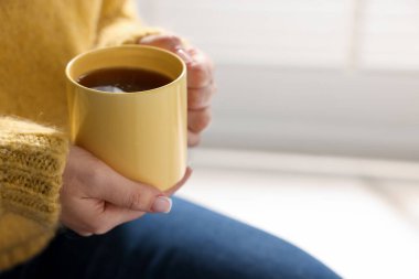 Kapalı mekanda çay içen boş sarı bardağı tutan kadın, yakın plan. Metin için boşluk
