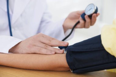 Hastanedeki masada kadının kan basıncını sphygmomanometre ile ölçen doktor, yakın plan.