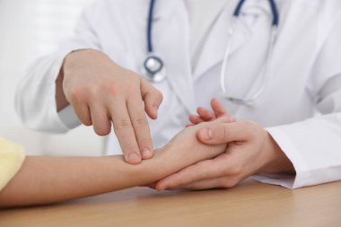 Doktor, klinikteki masada parmaklarıyla kadının nabzını kontrol ediyor.