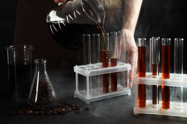 Siyah masada cam test tüpüne damlatan kadın, yakın plan.