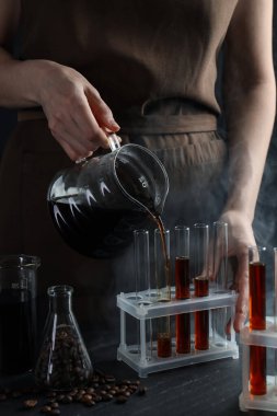 Siyah masada cam test tüpüne damlatan kadın, yakın plan.