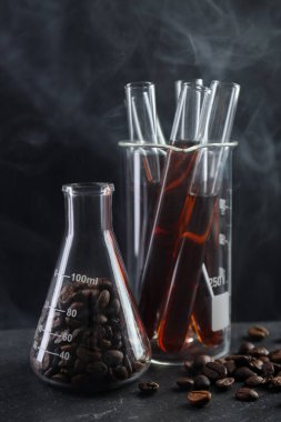 Kahve, fasulye ve dumanlı laboratuvar bardakları siyah masada, yakın plan.