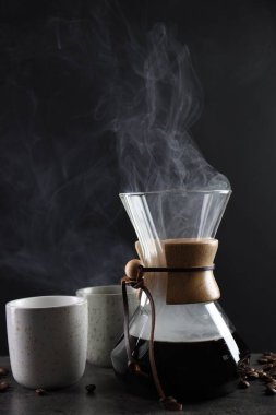 Cam kimya kahve makinesi, lezzetli kahve, fasulye ve fincanlar gri masada, yakın plan.