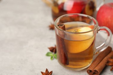 Aromatic fruit tea in glass cup, apple, mint and spices on grey table, closeup. Space for text