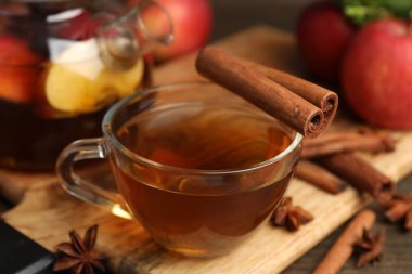 Aromatic fruit tea in glass cup, teapot, apples and spices on wooden table, closeup