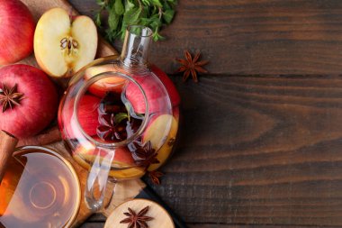 Aromatic fruit tea in glass teapot, cup, apples, mint and spices on wooden table, flat lay. Space for text