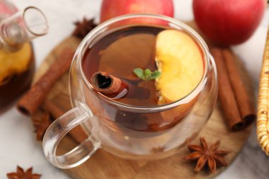 Cam fincanda aromatik meyve çayı, beyaz mermer masada elmalar ve baharatlar, yakın plan.