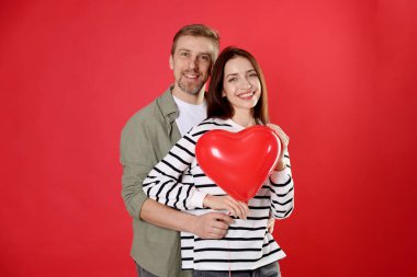 Kırmızı arka planda kalp şeklinde balonları olan mutlu bir çift. Sevgililer Günü kutlaması