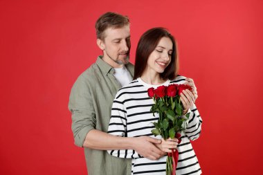 Kırmızı arka planda gül buketi olan mutlu bir çift. Sevgililer Günü kutlaması