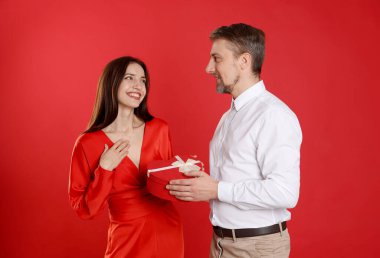 Mutlu adam kırmızı arka planda sevgililer günü hediyesiyle sevgilisine sürpriz yapıyor.