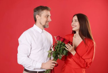 Kırmızı arka planda bir buket gülle kız arkadaşına sürpriz yapan bir adam. Sevgililer Günü kutlaması