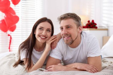 Yataktaki mutlu çift kalp şeklinde balonlarla süslenmiş. Sevgililer Günü kutlaması