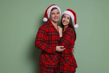 Gri yeşil arka planda Noel Baba şapkalı ve pijamalı mutlu bir çift. Noel atmosferi