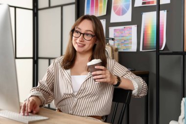 Kahveli tasarımcı masada bilgisayarla çalışıyor.