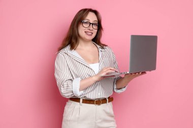 Pembe arka planda dizüstü bilgisayarı olan profesyonel tasarımcı.