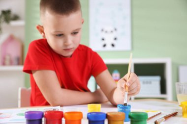 Masada fırçayla resim yapan sevimli bir çocuk, seçici bir odak.