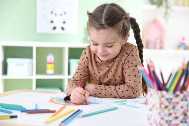 Masada kalemle çizen sevimli küçük kız.