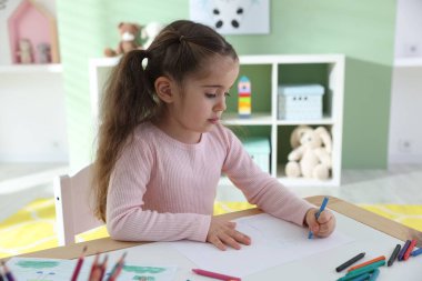 Masada pastel boyayla resim çizen sevimli küçük kız.