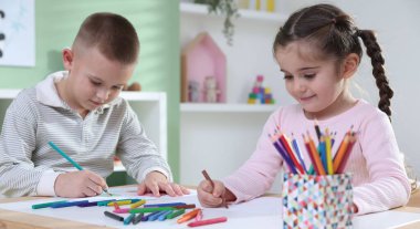 Children drawing with pencil and crayon at table indoors