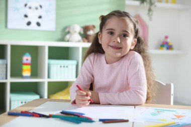 Masada pastel boyayla resim çizen sevimli küçük kız.