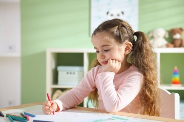 Masada pastel boyayla resim çizen sevimli küçük kız.