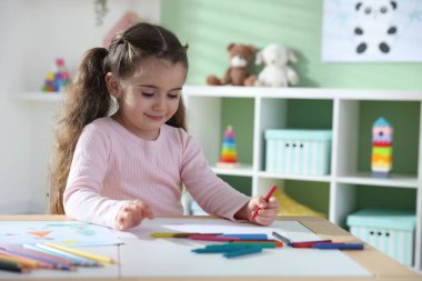 Masada pastel boyayla resim çizen sevimli küçük kız.