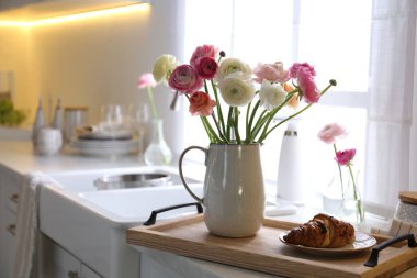 Güzel ranunculus çiçekli ahşap tepsi ve mutfakta taze kruvasan.