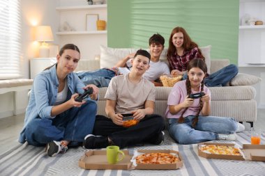 Video oyunu oynayan ve evde abur cubur yiyen bir grup genç.