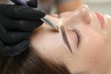 Güzellik uzmanı, kapalı mekanda kalıcı kaş makyajı prosedüründen önce kadının yüzüne işaretler çiziyor.