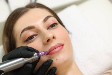 Güzellik uzmanı içeride genç bir kadına kalıcı dudak makyajı yapıyor, yakın plan. Metin için boşluk