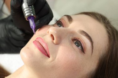 Güzellik uzmanı genç bir bayana kalıcı dudak makyajı yapıyor.