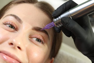 Güzellik uzmanı genç bir kadına kalıcı göz kalemi makyajı yapıyor.