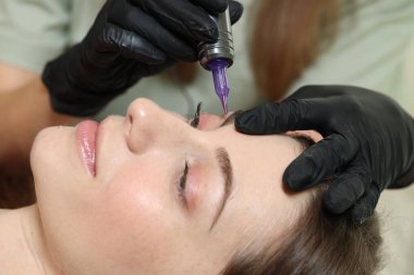 Güzellik uzmanı genç bayana kalıcı kaş makyajı yapıyor.