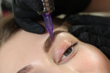 Güzellik uzmanı genç bayana kalıcı kaş makyajı yapıyor.